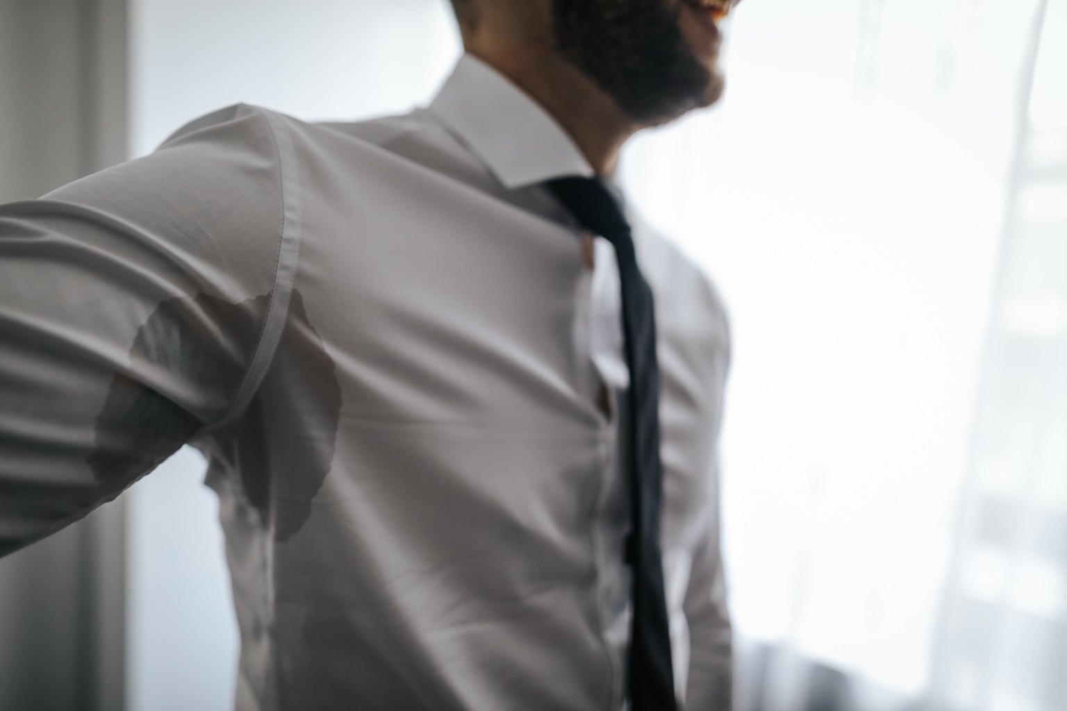 Man in a dress shirt with a visible underarm sweat stain from excessive sweating