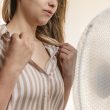 Woman in a striped shirt pulling her collar away from her skin to cool off in front of an electric fan